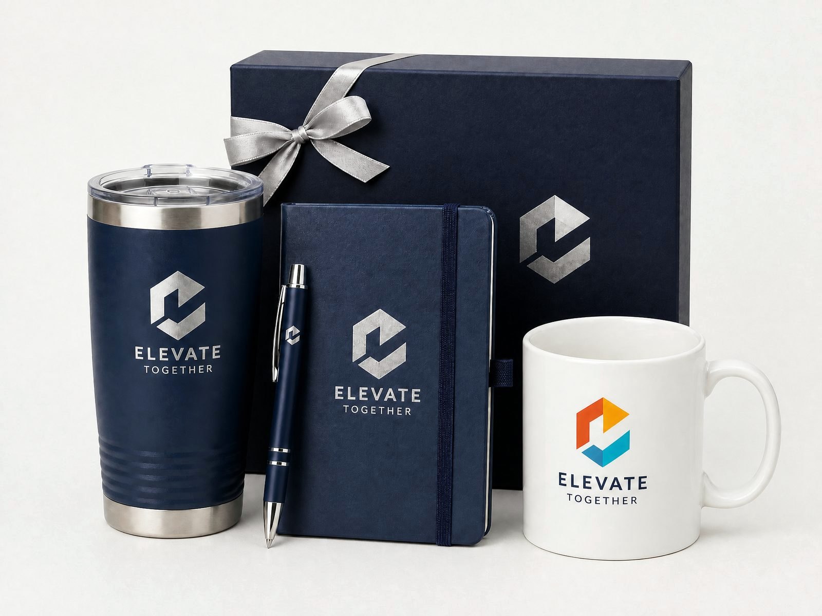 A branded corporate gift set: an insulated tumbler, a metal pen, a hardcover notebook and a ceramic mug in a ribboned gift box